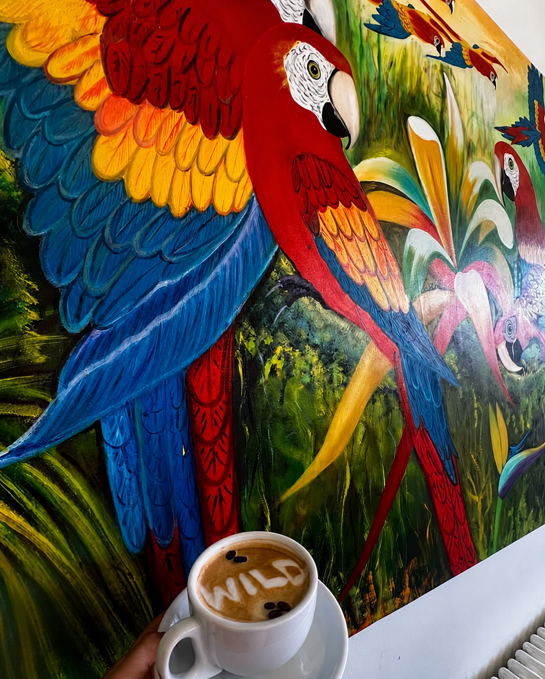 Latte art in front of the hand-painted macaw mural